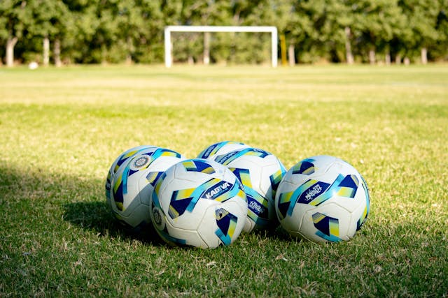 Varios balones de fútbol sobre el césped frente a una portería en un campamento de verano.