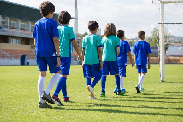 Grupo de niños futbolistas caminando juntos por el campo hacia la portería