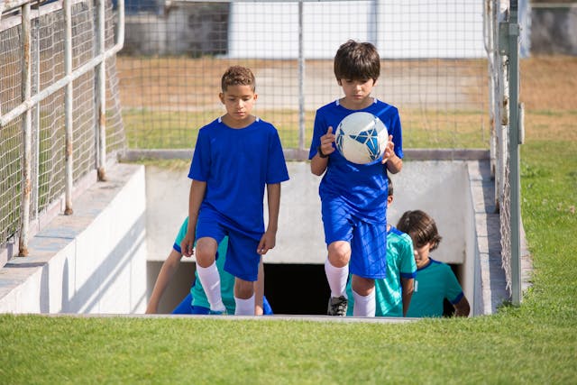 Niños futbolistas saliendo del túnel hacia el campo de juego con una pelota en las manos
