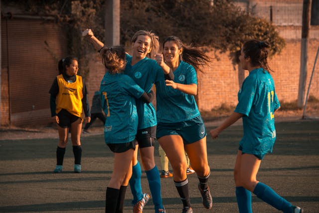 Jugadoras de fútbol femenino celebrando un gol durante un partido en una cancha al aire libre