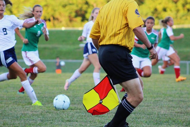 Ley Wenger: la nueva regla del fuera de juego en el fútbol Árbitro asistente levantando la bandera durante un partido de fútbol femenino, señalando posible fuera de juego