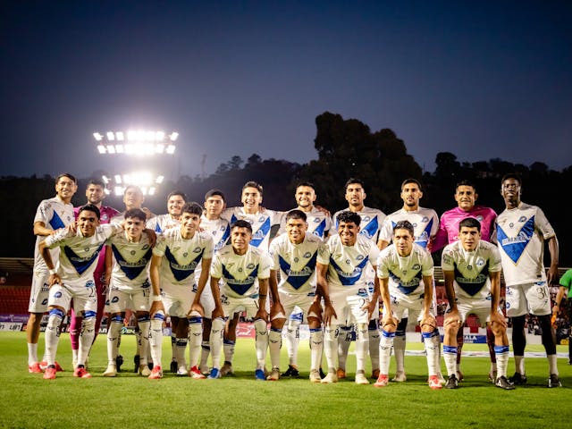 Equipo de fútbol posando en el campo antes de comenzar un partido nocturno bajo los reflectores del estadio.
