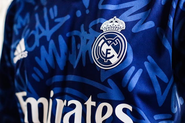 Camiseta de fútbol con escudo oficial y diseño moderno. Camiseta azul de un equipo de fútbol con detalles gráficos y escudo bordado en el pecho.